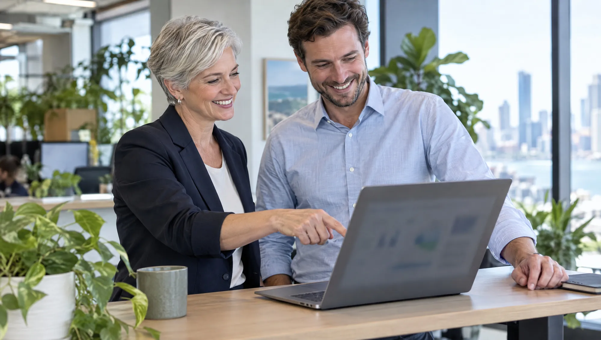 Two smiling managers look at a laptop together, one pointing at the screen.