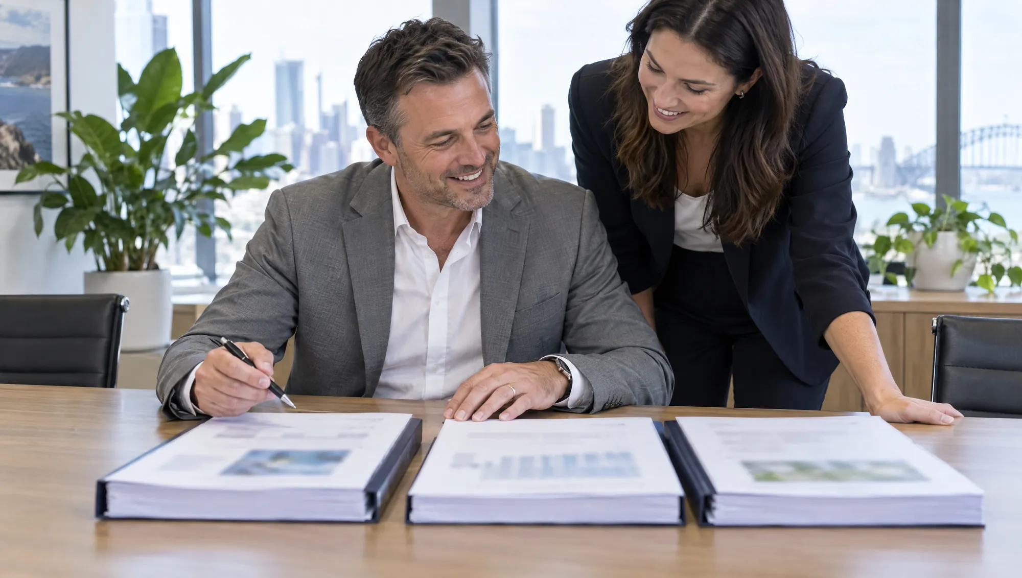 A smiling manager compares three bound proposals laid side by side on a table, with a colleague leaning in.