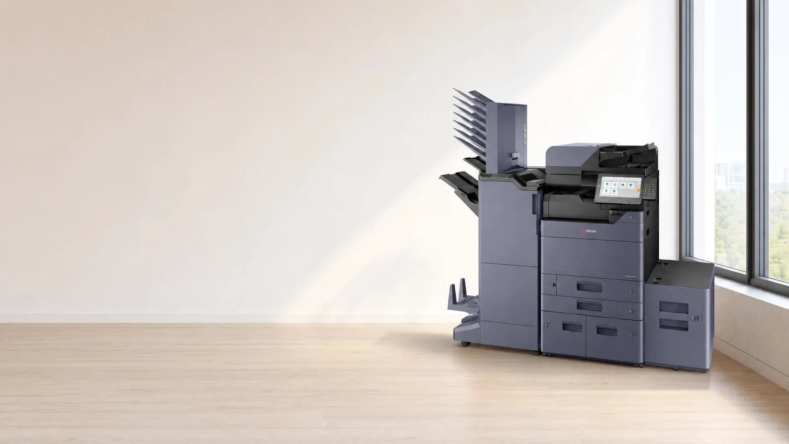 A Kyocera multifunction printer with a mailbox finisher and a high capacity side deck standing in an empty office, daylight from a window wall on the right