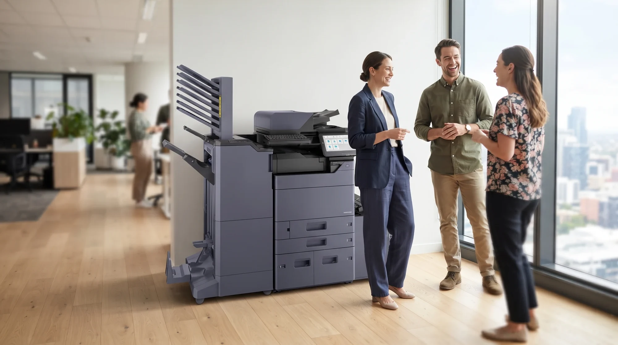 A Kyocera MZ2501ci with a finisher and a high capacity side deck in a bright open plan office, three colleagues talking beside it