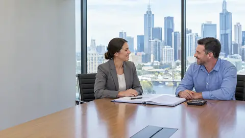 A woman from finance and a man from facilities smiling across a boardroom table with a bound agreement open between them, the city skyline through the glass behind