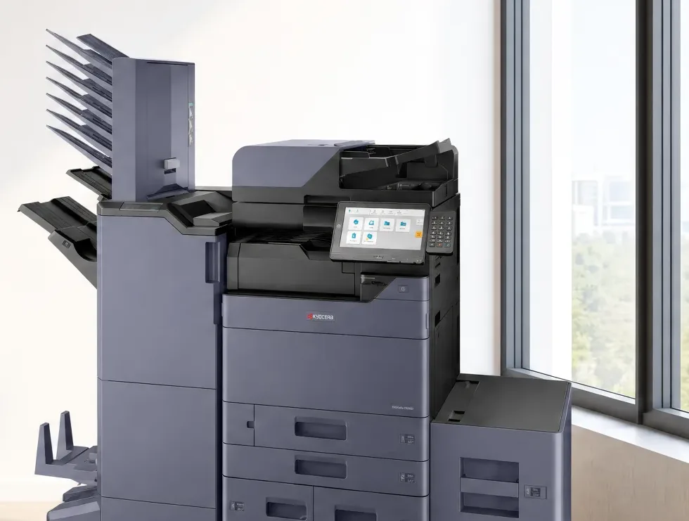 A Kyocera multifunction printer from the side, showing the finisher, the lit control panel, three paper drawers and the high capacity side deck