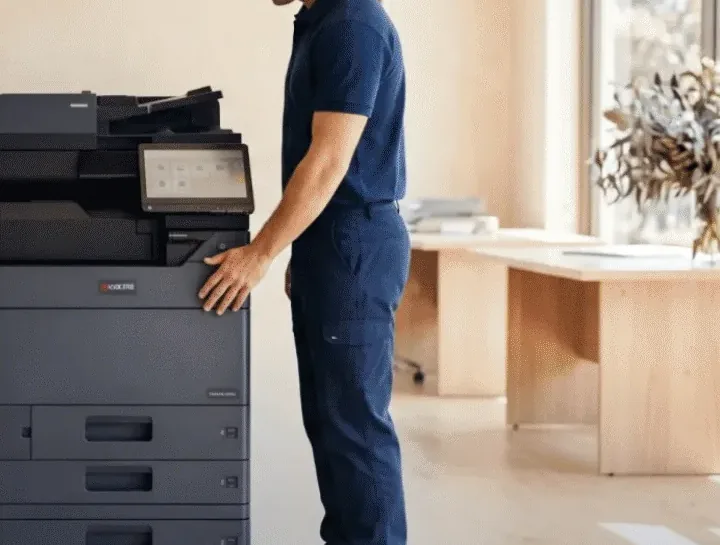 A technician’s hand resting on the front panel of a Kyocera multifunction printer, the touchscreen lit beside it